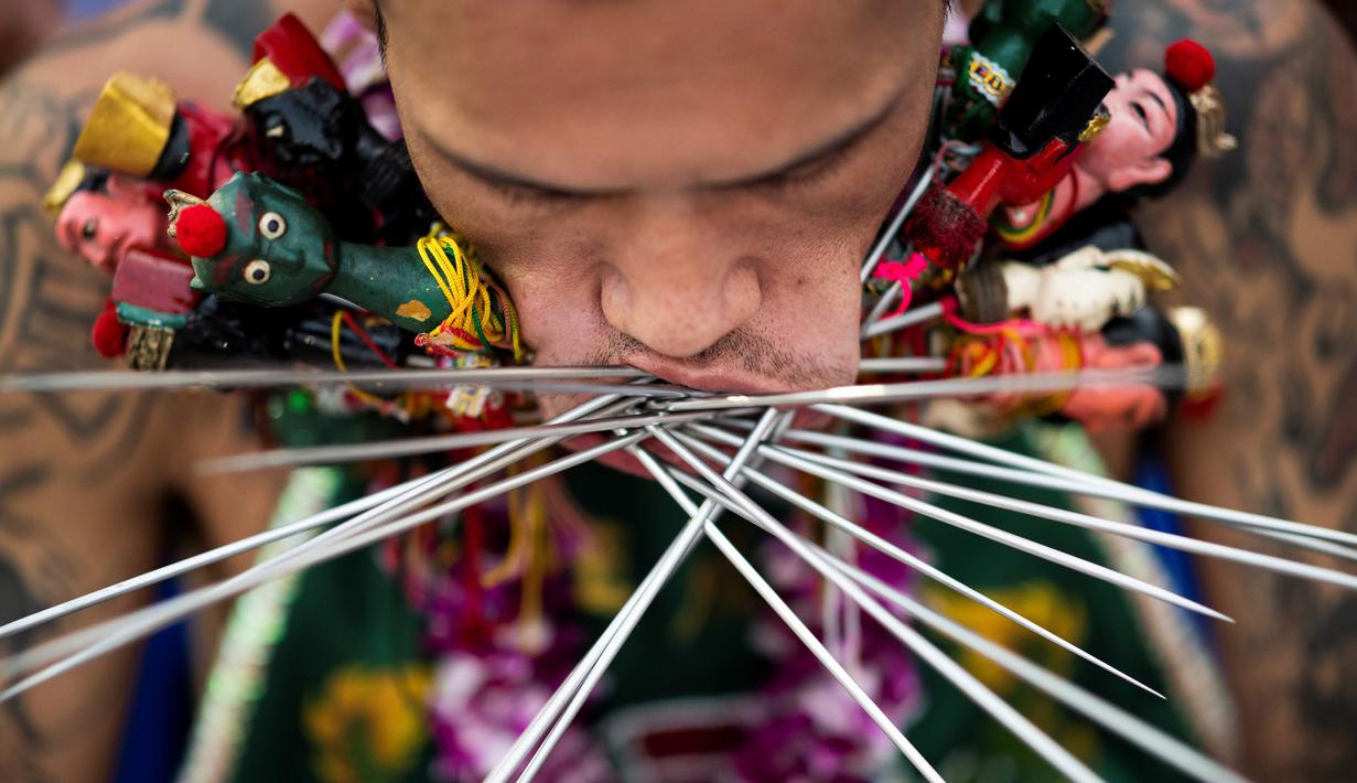 Penganut kuil Loem Hu Thai Su manusukkan besi tusuk satai ke pipinya saat festival vegetarian tahunan di Phuket, Thailand, Jumat (12/10). Sebelum mengikuti festival, semua peserta diharapkan tidak makan daging. (Jewel Samad/AFP)