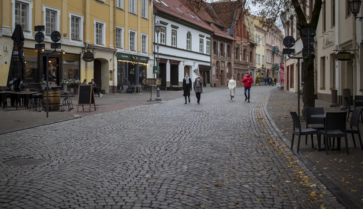 Penduduk lokal berjalan di Kota Tua yang kosong di Vilnius, Lithuania (7/11/2020). Seluruh wilayah telah dikunci selama tiga minggu secara nasional dari 7 November hingga 29 November, yang memberlakukan pembatasan pada kehidupan sosial dan kegiatan ekonomi.  (AP Photo/Mindaugas Kulbis)