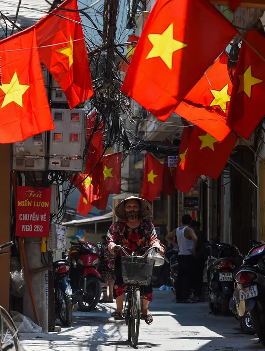 Seorang wanita mengendarai sepeda di sepanjang gang yang didekorasi dengan bendera nasional Vietnam menjelang perayaan Hari Nasional Vietnam di Hanoi (1/9/2020). Peringatan 75 tahun Hari Nasional Vietnam jatuh pada tanggal 2 September 2020. (AFP Photo/Nhac Nguyen)
