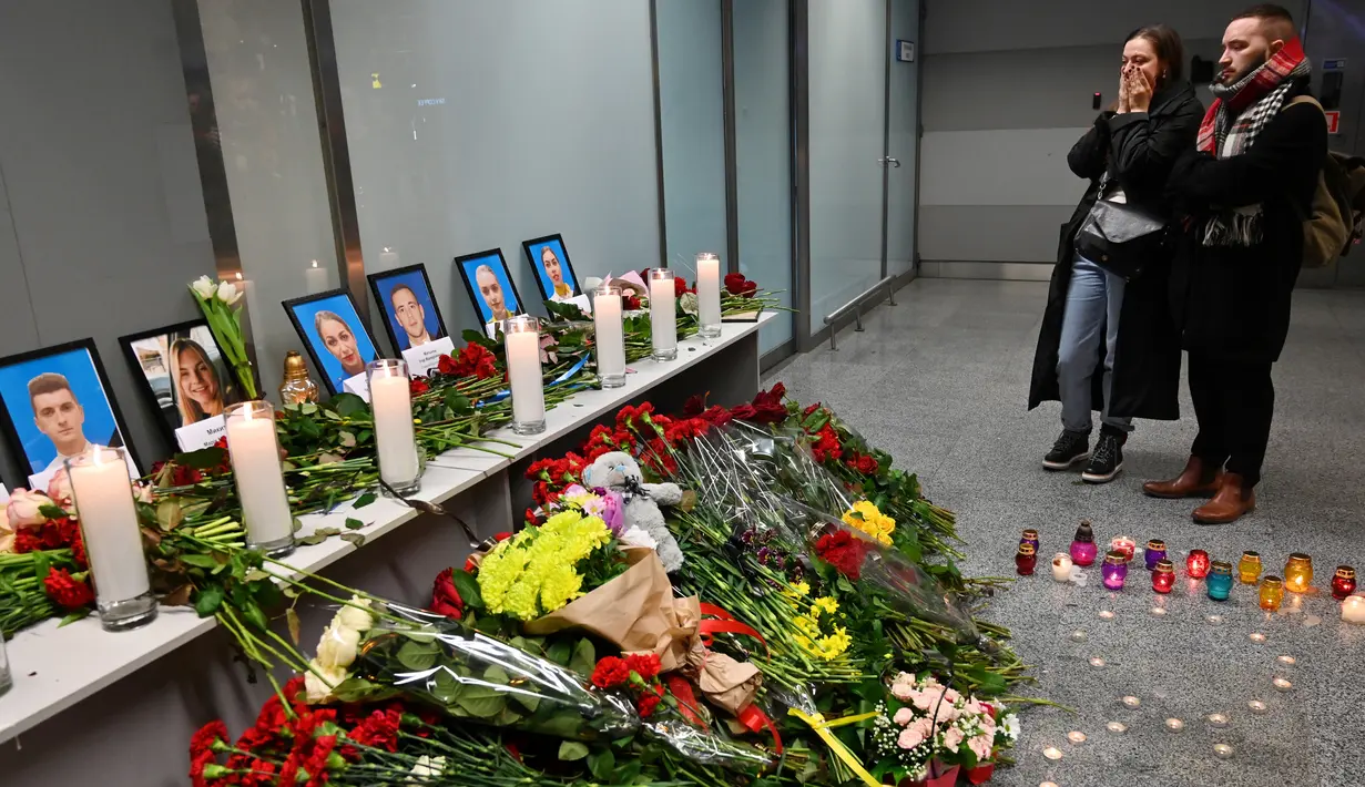Orang-orang memandangi foto para korban pesawat 737-800 Ukraina yang jatuh di Iran, di bandara internasional Borispil, Kiev, Rabu (8/1/2020). Pesawat yang membawa 176 orang itu jatuh setelah lepas landas dari bandara utama Teheran dan menewaskan semua penumpang. (Sergei SUPINSKY/AFP)