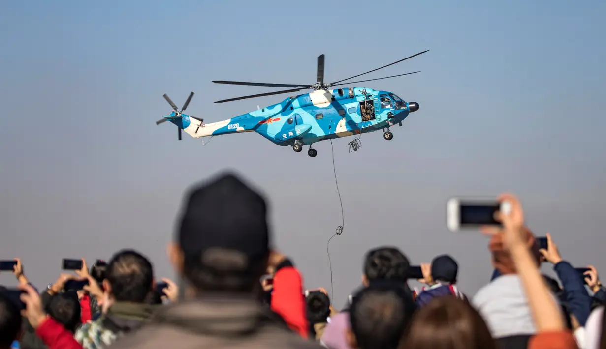 Penonton mengambil gambar helikopter serba guna Z-8 yang tampil dalam perayaan HUT ke-70 Angkatan Udara Tentara Pembebasan Rakyat di Changchun, Provinsi Jilin, Kamis (17/10/2019). Ada penerbangan aerobatik, pertunjukan parasut hingga demonstrasi pasukan khusus udara. (STR/AFP)
