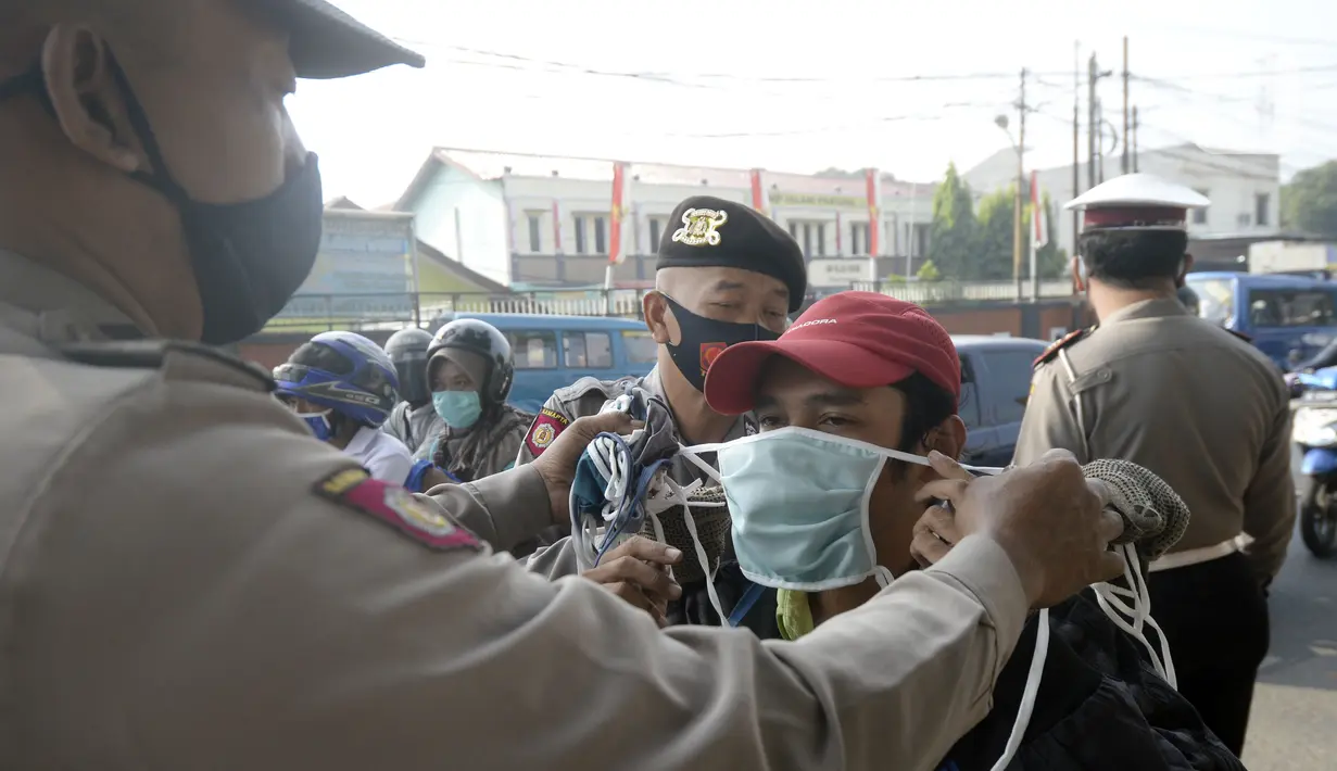 Anggota polisi dari Polsek Parung membantu memasangkan masker kepada pengendara sepeda motor di depan Polsek Parung, Kabupaten Bogor, Jawa Barat, Rabu (2/9/2020). Pembagian masker gratis setiap usai apel ini inisiatif anggota sejak masa pandemi COVID-19. (merdeka.com/Dwi Narwoko)