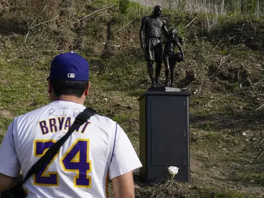 Oscar Romero berdiri dekat patung untuk mengenang Kobe Bryant dan putrinya, Gianna di Calabasas, California, Rabu (26/1/2022). Patung itu dibawa seniman Dan Medina, di jalan setapak dekat lokasi Bryant, putrinya dan tujuh orang lainnya tewas dalam kecelakaan helikopter pada 2020. (AP/Ashley Landis)