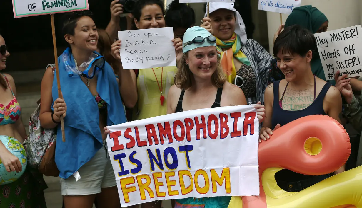 Sejumlah wanita mengenakan pakaian renang sambil memegang papan protes saat menggelar aksi di depan kedutaan Prancis di London, Inggris, Kamis (25/8). Mereka memprotes larangan burkini yang diberlakukan di kota-kota pesisir di Prancis. (REUTERS/Neil Hall)
