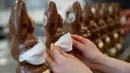 Pekerja menyiapkan cokelat paskah berbentuk kelinci yang mengenakan masker di toko roti Baeckerei Bohnenblust di Bern, Swiss, Jumat (27/3/2020). Cokelat paskah yang dibuat di tengah pandemi virus corona yang sedang merebak di seluruh dunia ini dijual sekitar RP 143 ribu. (STEFAN WERMUTH/AFP)