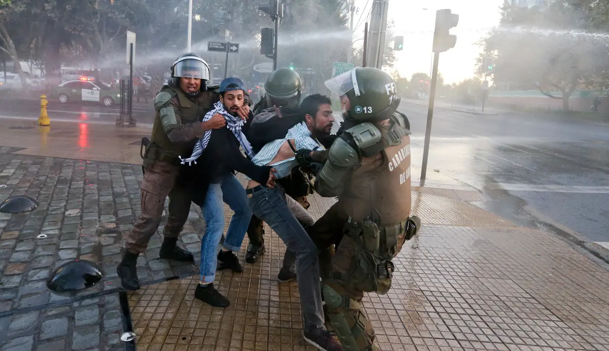 Polisi anti huru hara menarik dua orang pria saat terjadi unjuk rasa di luar kedutaan AS di Santiago, Chili (14/4). Serangan itu menyisakan puing-puing bangunan yang luluh lantak akibat rudal. (AP / Esteban Felix)