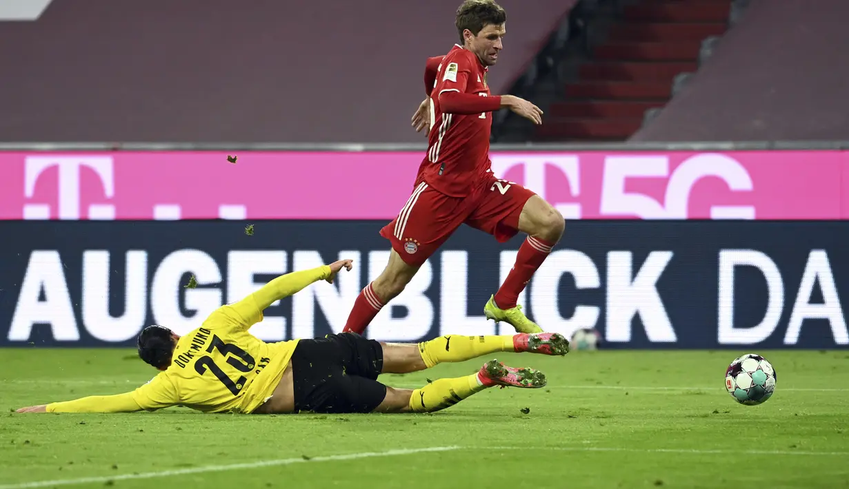 Gelandang Bayern Munchen, Thomas Mueller berusaha melewati gelandang Borrusia Dortmund, Emre Can pada pertandingan lanjutan Bundesliga Jerman di Allianz Arena di Munich, Minggu (7/3/2021). Berkat kemenangan ini Bayern mempertahankan posisi mereka di puncak klasemen. (Sven Hoppe/Pool via AP)