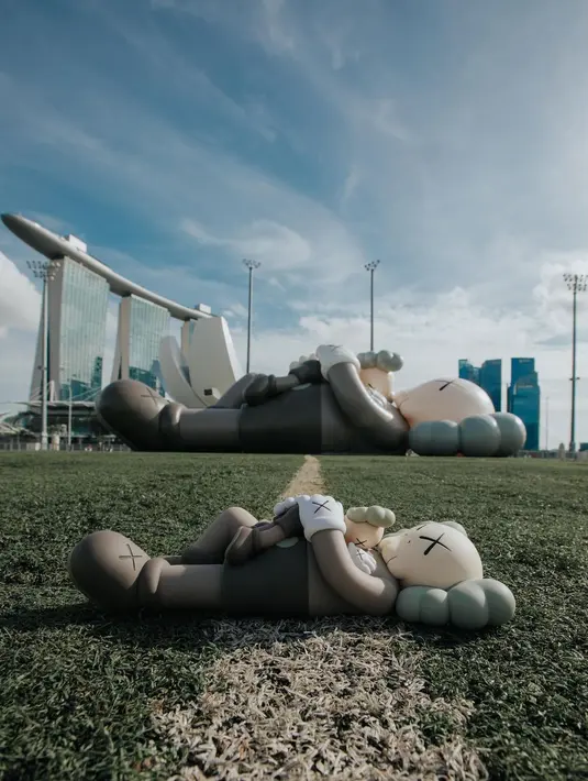 Setelah pandemi mulai mereda, KAWS: HOLIDAY terlihat berbaring sambil memeluk ‘anaknya’ dengan latar belakang Marina Bay Sands, Singapura pada November 2021. [Instagram/arr.allrightsreserved]
