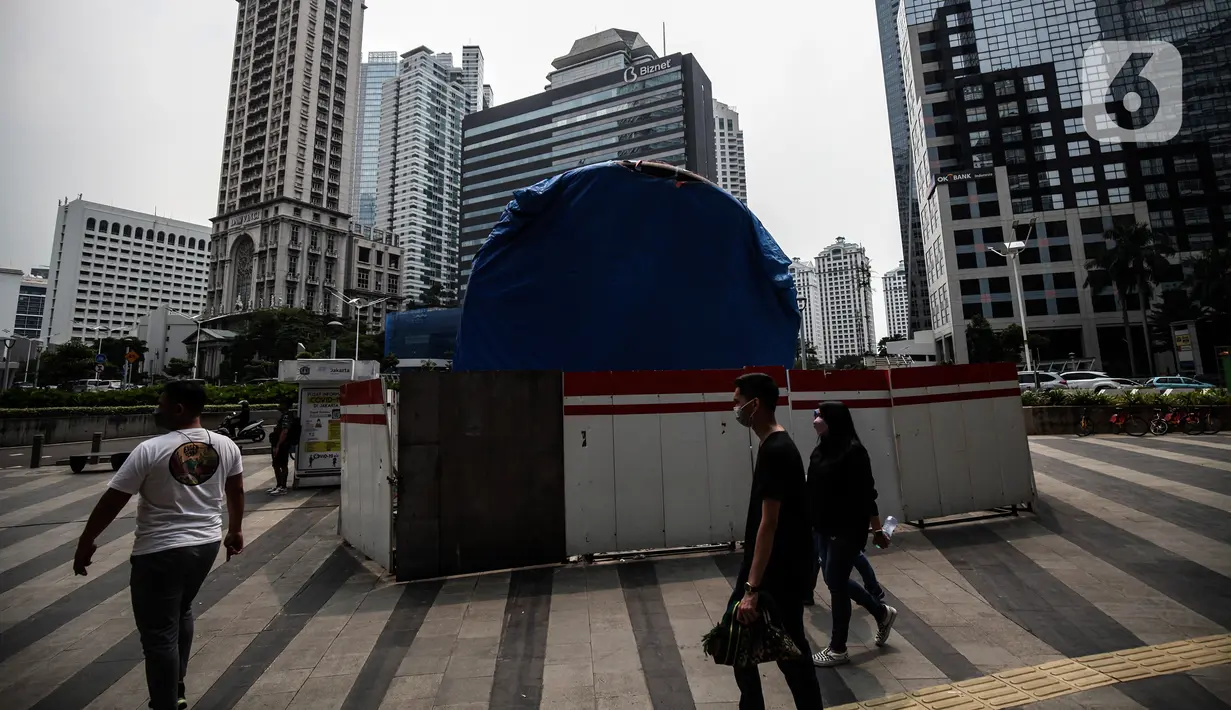 Warga melintas di dekat proyek Pembangunan tugu sepeda di Jalan Jenderal Sudirman, Jakarta, Rabu (30/3/2022). Tugu yang dulu sempat boming dan digembar-gemborkan kini terlihat terhenti pengerjaannya dan hanya ditutup terpal. (Liputa6.com/Johan Tallo)