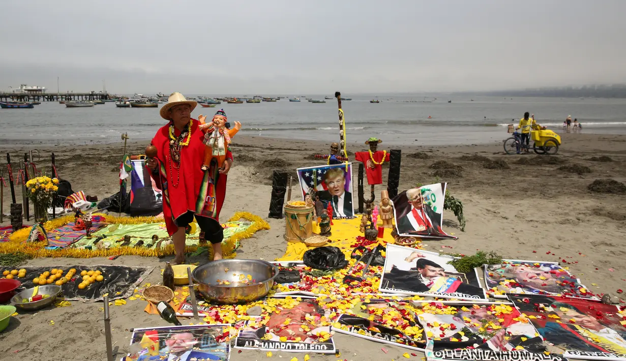 Seorang dukun menggelar ritual dengan meletakkan sejumlah poster bergambar para pemimpin dunia di Pantai Agua Dulce di Lima, Peru, (29/12). Para dukun ini meramalkan AS akan diselimuti dengan malapetaka dan kesuraman pada 2017. (Reuters/Mariana Bazo)