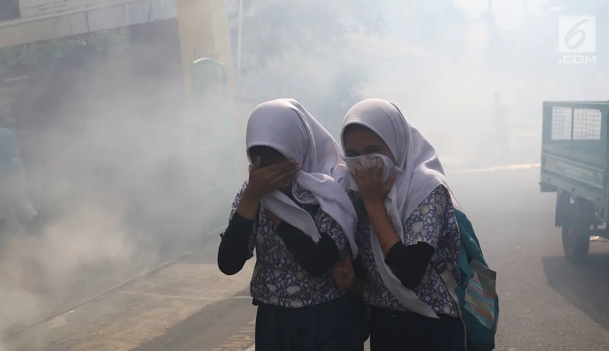 Dua siswi berlarian saat petugas melakukan pengasapan (fogging) di kawasan Kebon Baru, Tebet, Jakarta, Kamis (28/2). Pengasapan dilakukan terkait adanya warga di kawasan itu yang terkena penyakit demam berdarah (Liputan6.com/Immanuel Antonius)