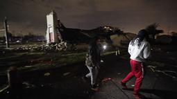 Breign Collins dan Darryl Bardell (kanan) berjalan melewati gereja yang hancur setelah tornado melanda daerah di Arabi, La., Selasa (22/3/2022). Tornado menerjang bagian New Orleans dan sekitarnya menghancurkan kabel listrik dan menyebarkan puing-puing di bagian kota. (AP Photo/Gerald Herbert)
