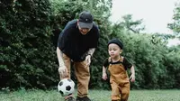 Ilustrasi ayah dan anak. (Photo by Ketut Subiyanto: https://www.pexels.com/photo/man-in-black-t-shirt-playing-with-boy-in-brown-overall-and-soccer-ball-4933837/)