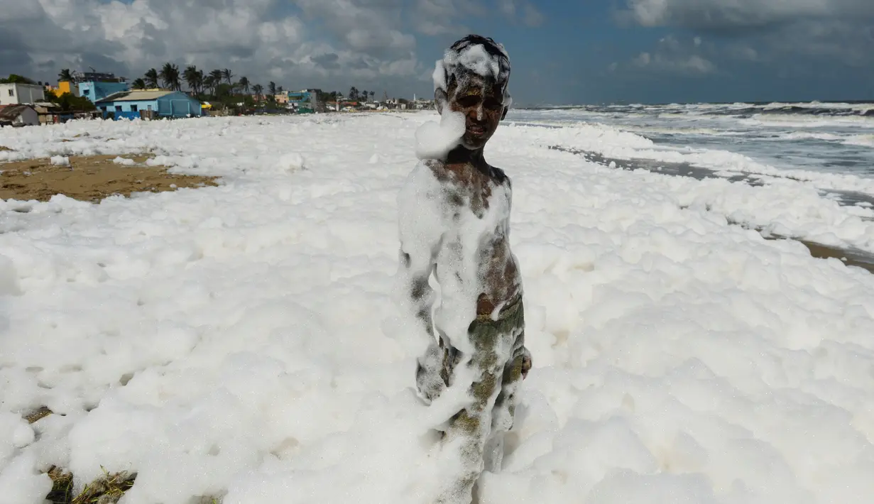 Seorang anak bermain limbah busa yang disebabkan polutan saat bercampur dengan ombak di pantai di Chennai (29/11/2019). Limbah mencapai laut melalui sungai, memicu busa beracun di pantai tersebut. (AFP/Arun Sankar)