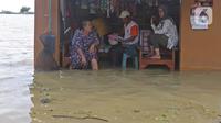 Warga berada di salah satu warung yang terendam banjir di Desa Sukalaksana Kabupaten Bekasi, Jawa Barat, Senin (22/02/2021). Jebolnya tanggul Sungai Citarum ini disebabkan oleh debit air yang tinggi. (Liputan6.com/Herman Zakharia)