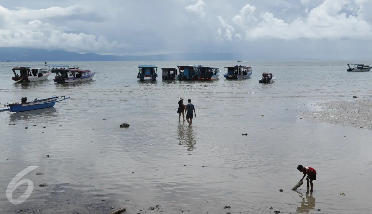 Sepasang wisatawan berjalan menuju kapal penumpang sementara seorang anak (kanan) bermain di pinggir pantai Pulau Bunaken, Manado, Sabtu (17/12). Taman Nasional Bunaken ini memiliki keindahan alam dan biota laut. (Liputan6.com/Fery Pradolo)