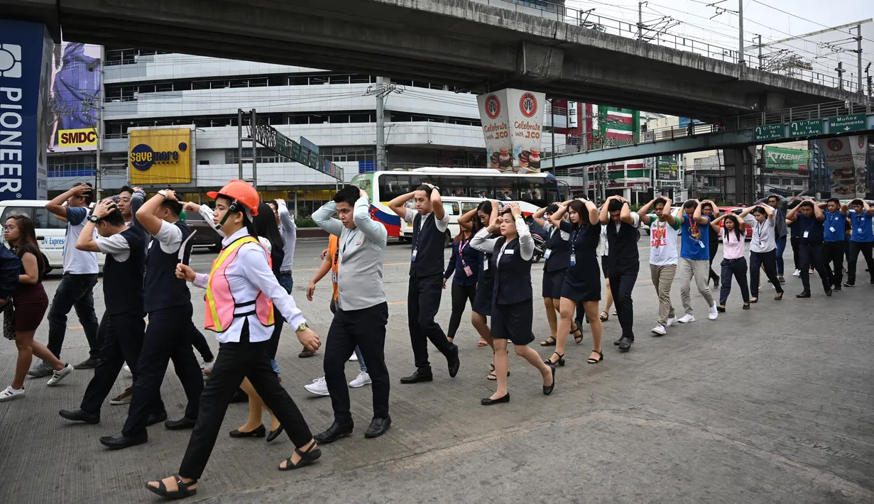 Karyawan pusat perbelanjaan melindungi kepalanya sambil berjalan saat mengikuti latihan gempa di Manila (14/11/2019). Latihan ini sebagai bagian dari kesiapsiagaan nasional menyusul berbagai gempa yang melanda pulau Mindanao bulan lalu. (AFP Photo/Ted Aljibe)