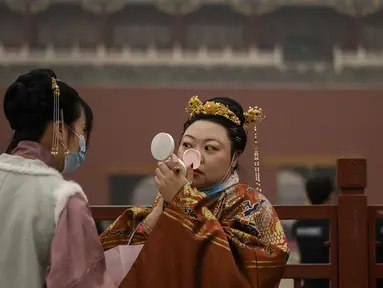 Seorang wanita dengan pakaian tradisional memeriksa riasannya saat dia berdiri di pintu masuk ke Kota Terlarang pada hari kedua Tahun Baru Imlek di Beijing (13/2/2021). Tahun Baru Imlek menandai Tahun Sapi pada 12 Februari. (AFP Photo/Noel Celis)
