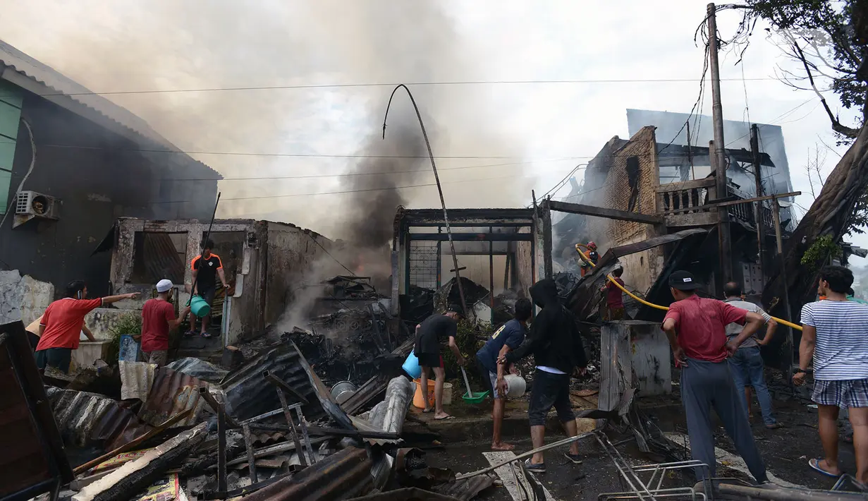 Warga membantu petugas pemadam kebakaran melakukan pendinginan rumah dan kios yang terbakar di Jalan Minangkabau, Jakarta, Selasa (7/7/2020). Delapan unit mobil pemadam kebakaran dikerahkan untuk memadamkan api yang hingga saat ini belum diketahui penyebab kebakaran. (merdeka.com/Imam Buhori)