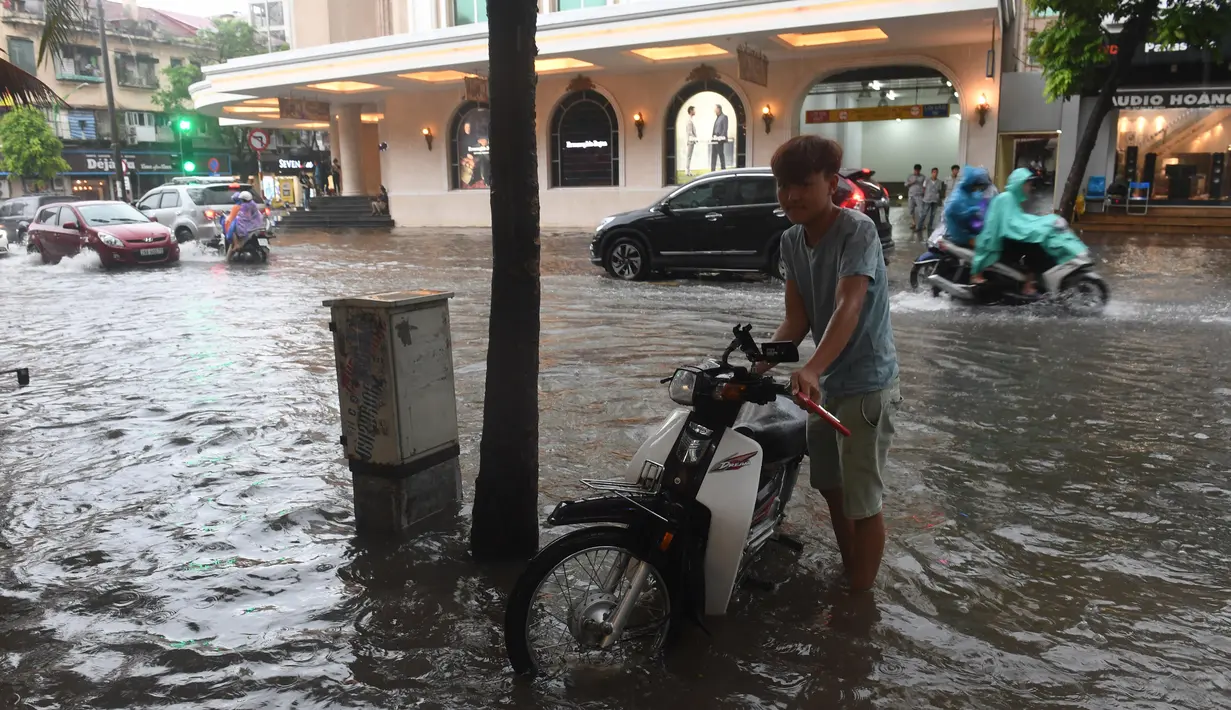 Warga mendorong motornya saat melintasi banjir setelah badai tropis Talas terjadi di Hanoi, Vietnam utara (17/7). (AFP Photo/Hoang Dinh Nam)