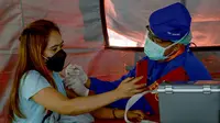 Seorang wanita menerima vaksin virus corona COVID-19 AstraZeneca di Denpasar, Bali, Sabtu (26/6/2021). Ratusan warga terlihat antusias mengikuti vaksinasi massal tersebut. (SONY TUMBELAKA/AFP)