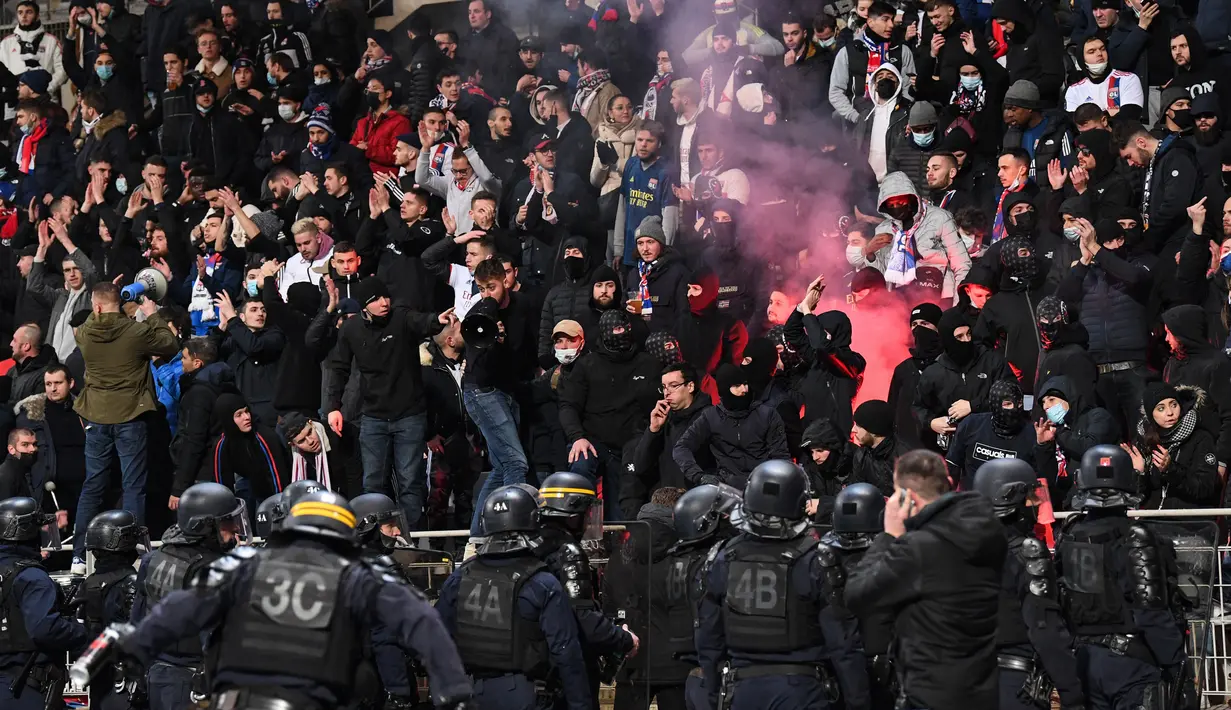 Polisi anti huru hara Prancis tiba ketika para penonton menyalakan suar pada pertandingan 64 besar Piala Prancis antara Paris FC dan Olympique Lyon di stadion Charlety, Jumat (17/12/2021). Pendukung saling bertarung dan beberapa dari mereka turun ke lapangan dan melemparkan suar. (Bertrand GUAY/AFP)