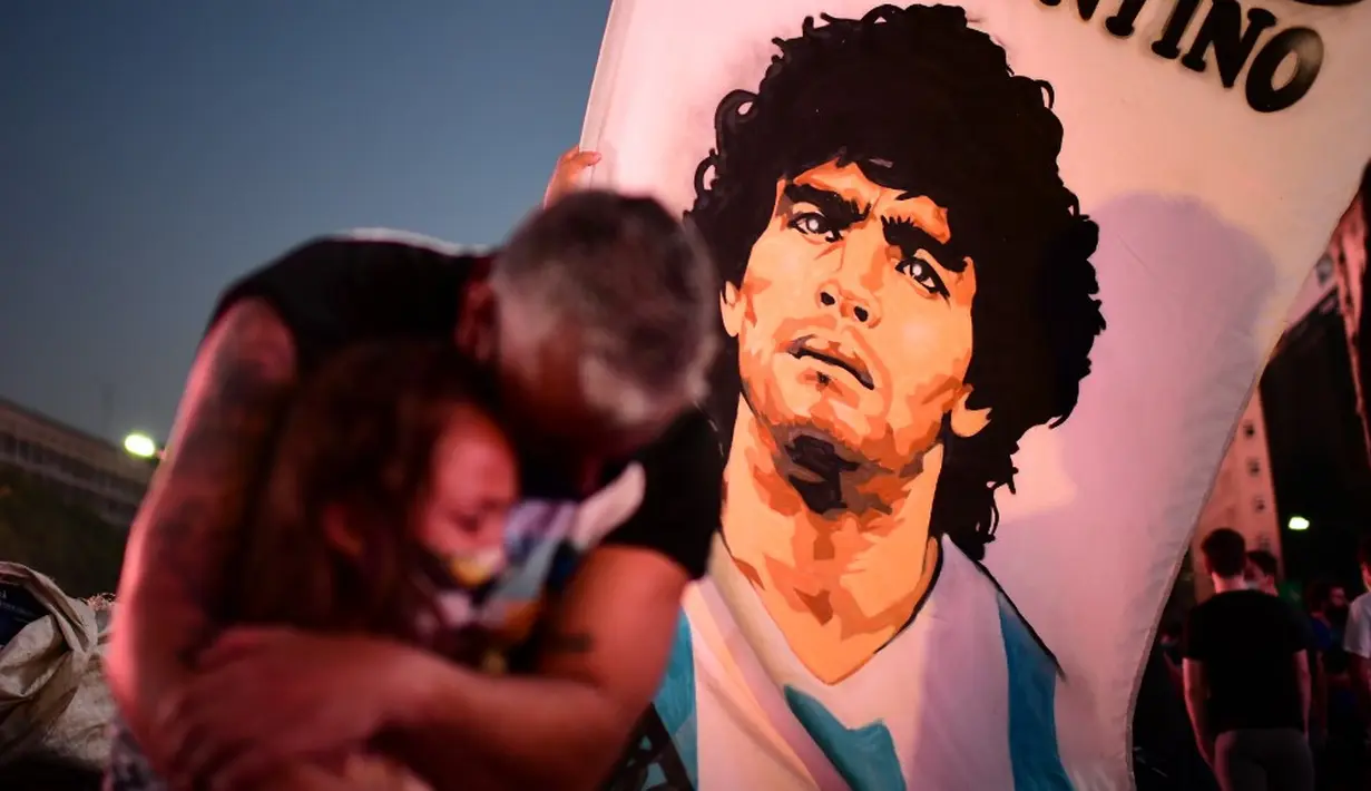 Fans legenda sepak bola Argentina Diego Maradona seorang ayah dan putrinya berduka saat mereka berkumpul untuk memberi penghormatan pada hari kematiannya di Obelisk, Buenos Aires, Argentina, 25 November 2020. (RONALDO SCHEMIDT/AFP)
