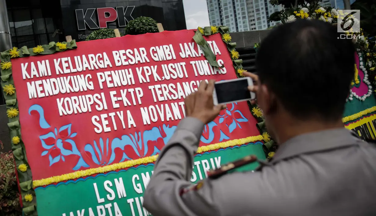 Petugas mengambil gambar karangan bunga berisi dukungan pada KPK di halaman Gedung KPK, Jakarta, Senin (20/11). Karangan bunga tersebut sebagai bentuk dukungan masyarakat kepada KPK terhadap pemberantasan kasus korupsi e-KTP. (Liputan6.com/Faizal Fanani)