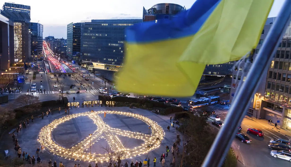 Bendera Ukraina berkibar ditiup angin saat tanda perdamaian raksasa dipasang para demonstran jelang KTT Uni Eropa dan NATO di Brussels, Belgia, 22 Maret 2022. Pengunjuk rasa meminta para pemimpin Uni Eropa memberlakukan larangan penuh terhadap bahan bakar Rusia. (AP Photo/Geert Vanden Wijngaert)