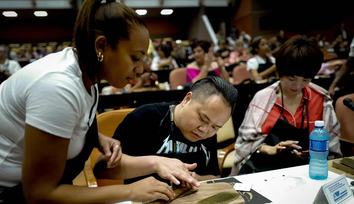 Seorang instruktur Kuba (kiri) membantu peserta menggulung cerutu selama kelas master dalam Festival Havana Cigar ke-20 di Istana Konvensi di Havana, Kuba (28/2). (AFP Photo/Adalberto Roque)