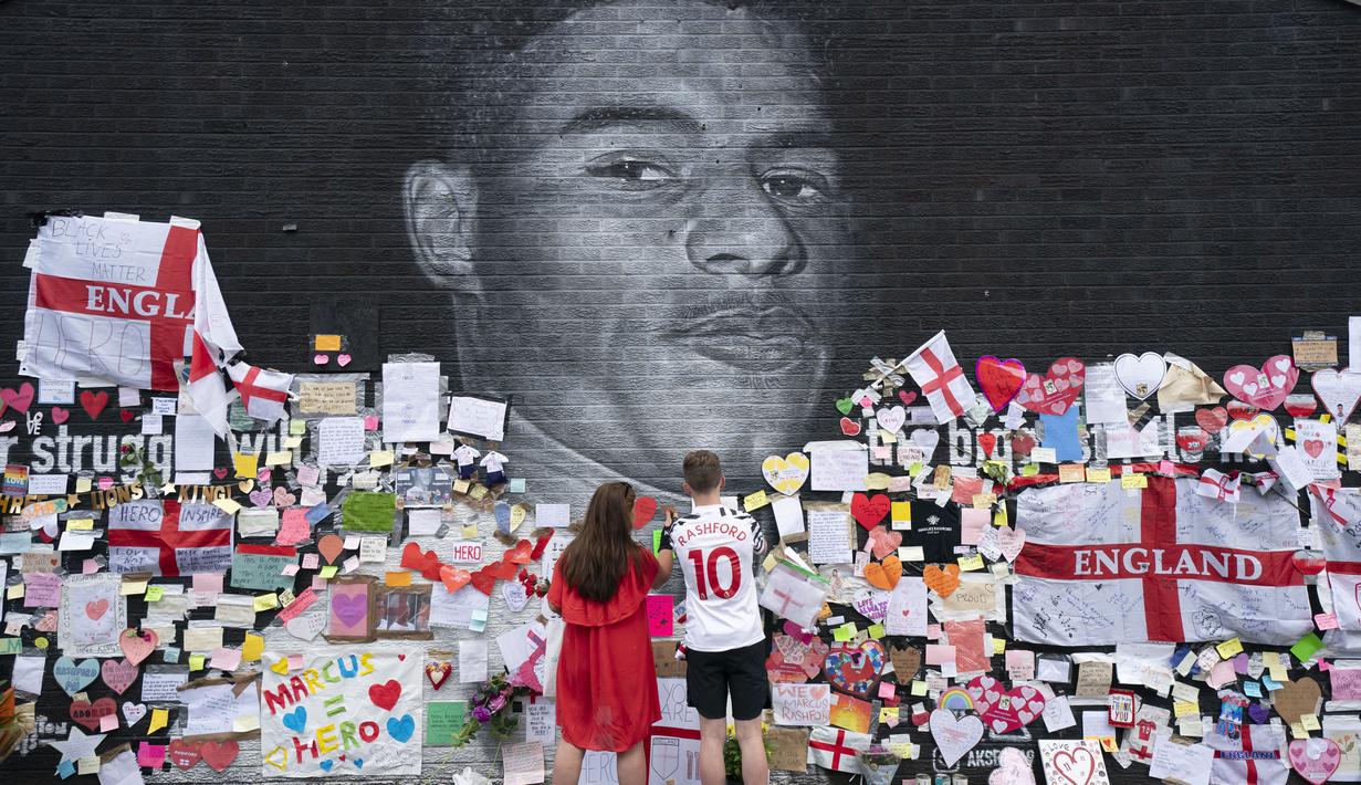 Sejumlah orang tampak menempelkan pesan dukungan dan meletakkan karangan bunga hingga pernak-pernik timnas Inggris di depan mural tersebut. (Foto:AP/Jon Super)