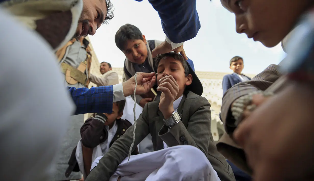 Seorang pria Yaman mengoleskan kosmetik tradisional Kohl ke kelopak mata remaja selama bulan puasa Ramadhan di Masjid Sanaa (16/4/2021).  Di Yaman, salah satu tradisi khas menandai Ramadhan yang masih lestari adalah aksi para pemuda yang merias mata dengan kohl. (AFP/ Mohammed Huwais)