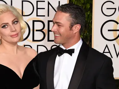 Lady Gaga ditemani Taylor Kinney menghadiri acara Golden Globes 2016 di Beverly Hilton Hotel, California, Minggu (10/1). Kompak mengenakan gaun bernuansa hitam, sang Mother Monster menggandeng mesra sang tunangan. (Jason Merritt/Getty Images/AFP)