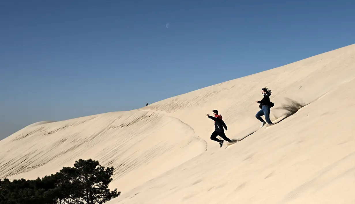 Seorang anak laki-laki dan perempuan berlari menyusuri gundukan pasir tertinggi di Eropa yang disebut "Dune du Pilat" di La Teste-de-Buch, Prancis pada 3 April 2021. The Dune of Pilat memiliki keunikan, yakni bukitnya dapat bergerak hingga mencapai 4,9 meter per tahunnya. (Philippe LOPEZ / AFP)