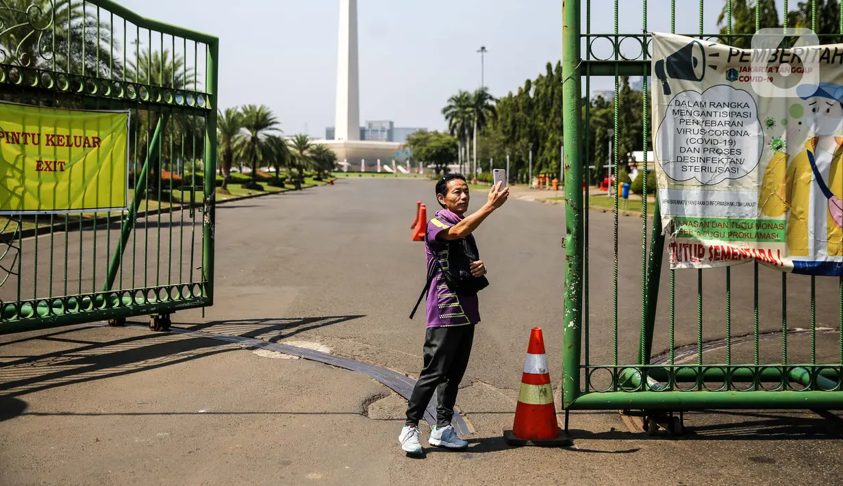 Warga berswafoto di depan kawasan Monumen Nasional (Monas), Jakarta, Minggu (26/7/2020). Sejumlah warga mulai mengunjungi kawasan Monas meski masih ditutup sementara di masa PSBB transisi. (Liputan6.com/Faizal Fanani)