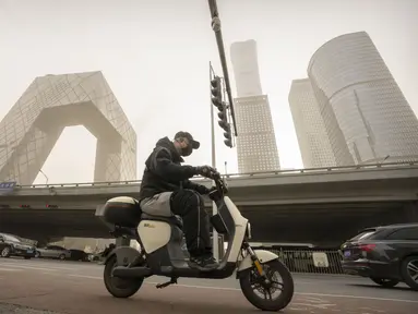 Seorang pria yang mengenakan masker mengendarai skuter di sepanjang jalan di kawasan pusat bisnis di Beijing, Rabu, 22 Maret 2023. (AP Photo/Mark Schiefelbein)
