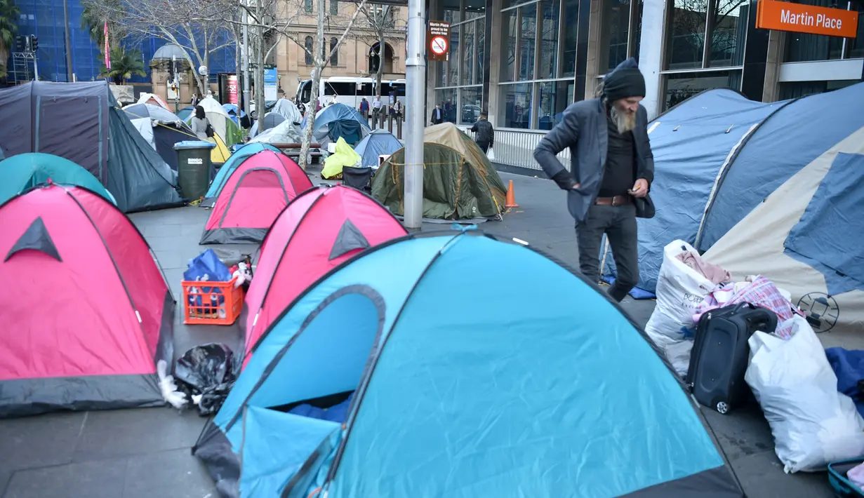 Seorang pria berjalan di antara tenda-tenda yang didirikan para tunawisma di kawasan Martin Place, pusat kota Sydney, Rabu (9/8). Pemerintah New South Wales menegaskan pihaknya akan menutup perkampungan tenda para tunawisma itu. (PETER PARKS / AFP)