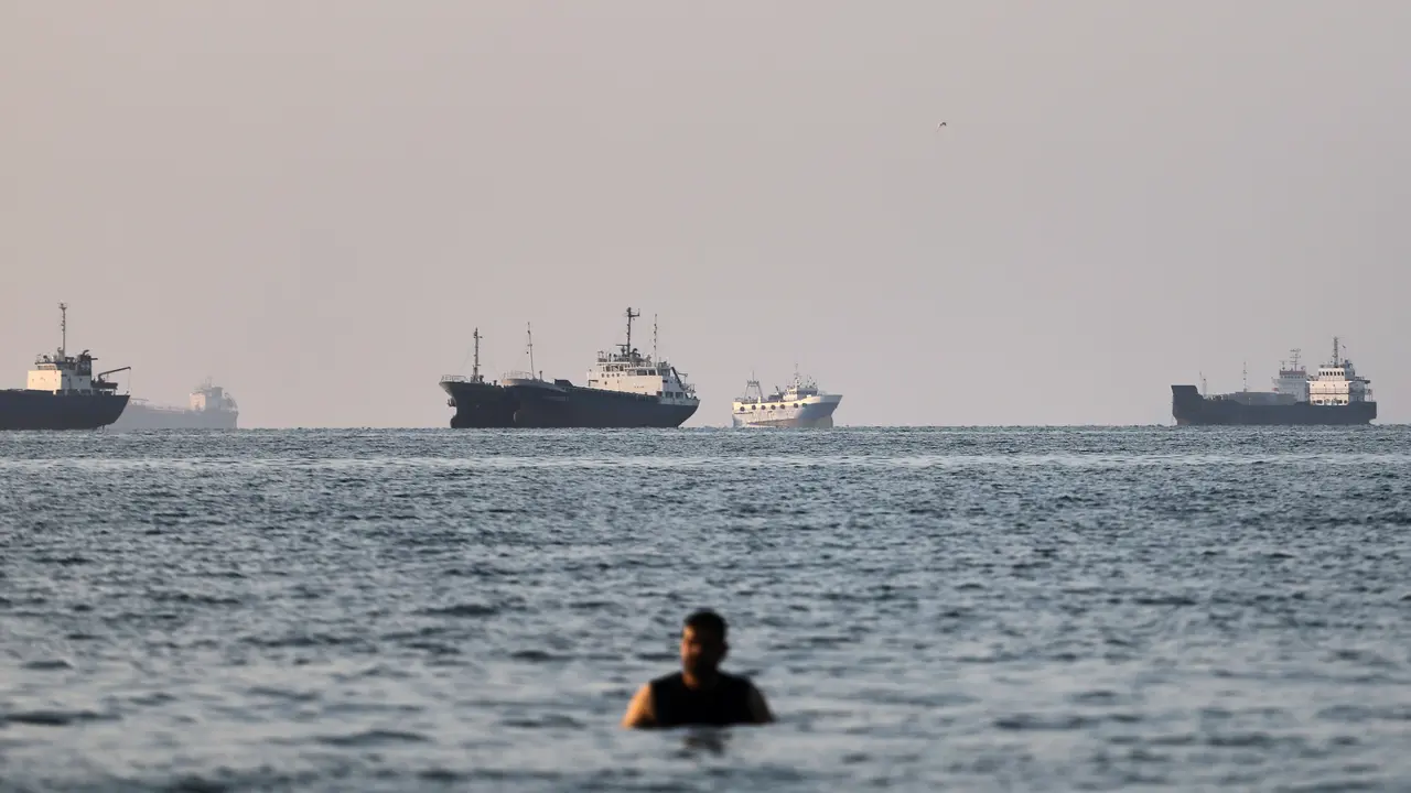 Seseorang berdiri di perairan dangkal saat kapal kargo dan kapal komersial berlabuh di Selat Hormuz di lepas pantai Bandar Abbas, Iran, Senin, 8 Juni 2026. (Amirhosein Khorgooi/ISNA via AP)