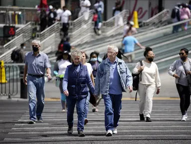 Pejalan kaki dengan masker dan tanpa masker berjalan melintasi Las Vegas Boulevard, di Las Vegas Selasa (27/4/2021). Warga Amerika Serikat (AS) yang telah menerima vaksin COVID-19 tidak lagi diwajibkan mengenakan masker saat berada di luar ruangan jika tidak ada kerumuman. (AP Photo/John Locher)