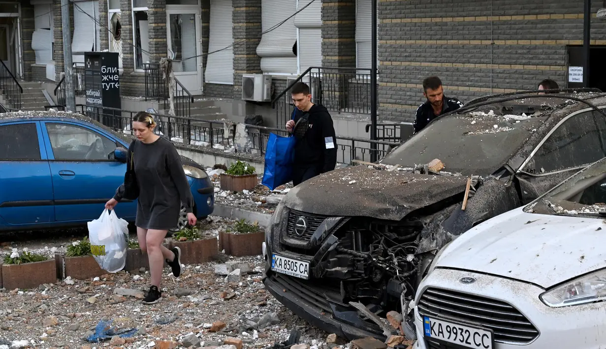 Penduduk setempat membawa barang-barang saat mereka meninggalkan bangunan tempat tinggal bertingkat, yang sebagian hancur setelah serangan pesawat tak berawak pada malam hari di Kyiv pada 30 Mei 2023. (Sergei SUPINSKY/AFP)
