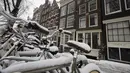 Sepeda yang tertutup salju diparkir di luar rumah kanal di pusat kota Amsterdam, saat salju dan angin kencang menyelimuti sebagian besar wilayah Belanda, Minggu (7/2/2021). Badai salju dengan suhu mencapai minus 10 derajat celsius membuat transportasi umum tidak beroperasi. (AP Photo/Peter Dejong)