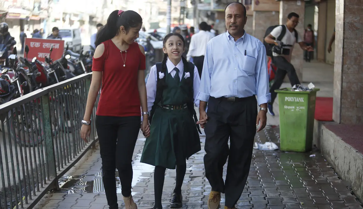Mantan Dewi Nepal atau Kumari, Matina Shakya (tengah) berjalan ke sekolah ditemani ayahnya Pratap Man Shakya (kanan) dan saudarinya di Kathmandu (9/10). Sewaktu menjadi Kumari, Matina dirawat oleh pengasuh yang ditunjuk secara khusus.(AFP Photo/Gopen Rai)