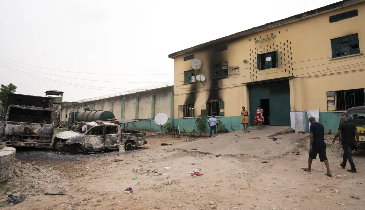 Orang-orang berjalan melewati kendaraan yang terbakar di depan sebuah fasilitas pemasyarakatan seusai serangan oleh kelompok bersenjata di Owerri, Nigeria, Senin (5/4/2021). Enam tahanan dilaporkan telah kembali, dan 35 tahanan lainnya menolak untuk melarikan diri. (AP Photo/David Dosunmu)