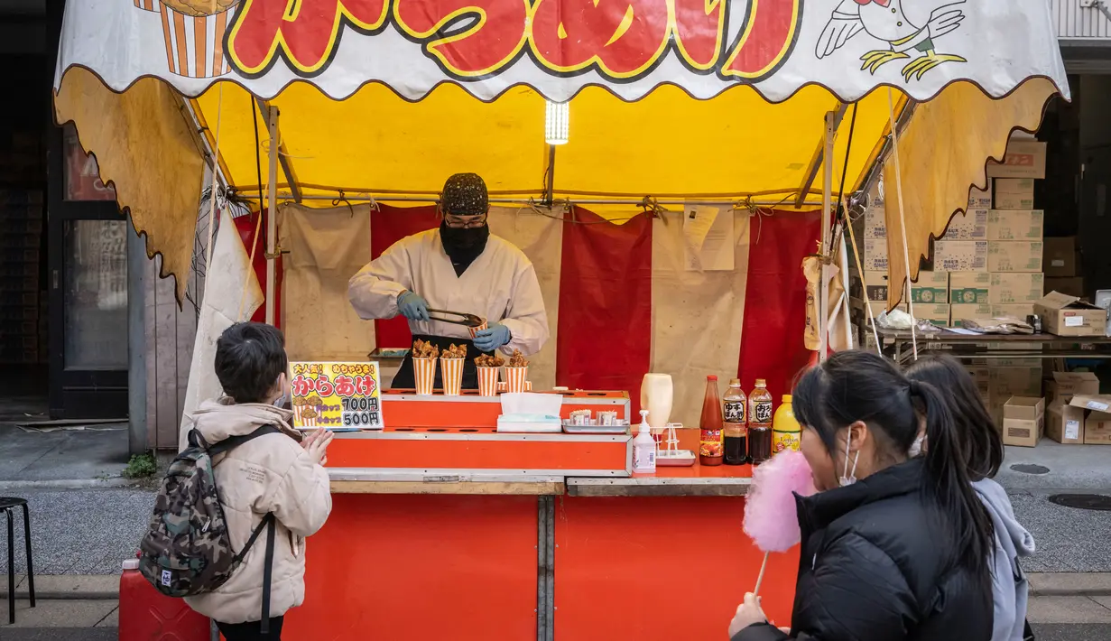 Seorang anak membeli ayam goreng pada kios makanan selama pekan raya akhir tahun di Distrik Nihonbashi, Tokyo, Jepang, 26 Desember 2022. Tak hanya menyuguhkan pemandangan indah dan makanan yang lezat, Jepang juga menjadi negara yang tepat untuk merayakan tahun baru. (Yuichi YAMAZAKI/AFP)