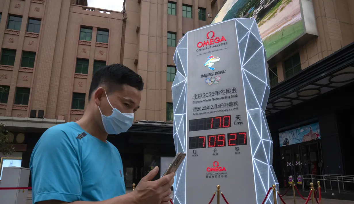 Orang-orang yang memakai masker untuk melindungi diri dari COVID-19 berjalan melewati layar yang menunjukkan jam hitung mundur ke Olimpiade Musim Dingin 2022 di Beijing (18/8/2021).  Kurang dari 200 hari lagi, meskipun masih belum jelas apakah penonton akan diizinkan. (AP Photo/Mark Schiefelbein)