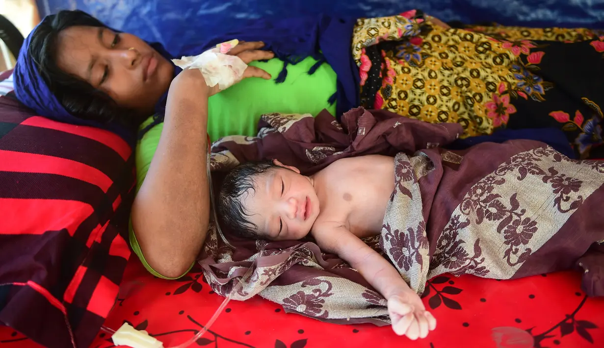Wanita Rohingya bernama Hasina Aktar terbaring bersama bayinnya usai melahirkan di kamp pengungsian Kutupalong (11/10). Anak Hasina Aktar ini diberi nama Mohammed Jubayed. (AFP Photo/Munir Uz Zaman)