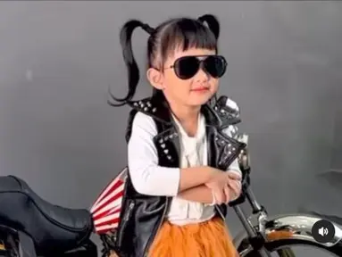 Bergaya seperti geng motor,  Khalisa Aghnia Bahira mengenakan rompi hitam, kacamata gelap berpose dengan latar belakang motor Harley Davidson berukuran mini. (Foto: Instagram/@kartikaputriworld)