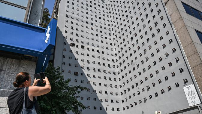 Pejalan kaki mengambil gambar pameran seni kontemporer yang meletakkan  sepatu perempuan di dinding sebuah bangunan di Istanbul, Selasa (17/9/2019). Sebanyak 440 sepatu melambangkan perempuan yang dibunuh oleh pasangan dan suami mereka di Turki sepanjang tahun 2018. (Ozan KOSE/AFP)