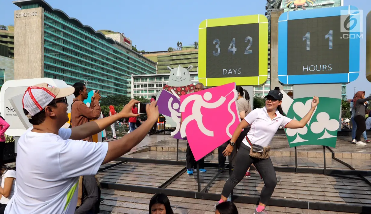 Seorang warga difoto dengan gaya berlari di layar Countdown Asian Games 2018 saat Car Free Day di Bundaran HI, Jakarta, Minggu, (10/09). Asian Games akan berlangsung pada 18 Agustus hingga 2 September 2018. (Liputan6.com/Fery Pradolo)