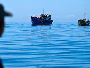 Seorang pria di atas kapal melihat para pengungsi Rohingya yang berlabuh di lepas pantai Labuhan Haji, Aceh Selatan, pada Selasa 22 Oktober 2024. (CHAIDEER MAHYUDDIN/AFP)